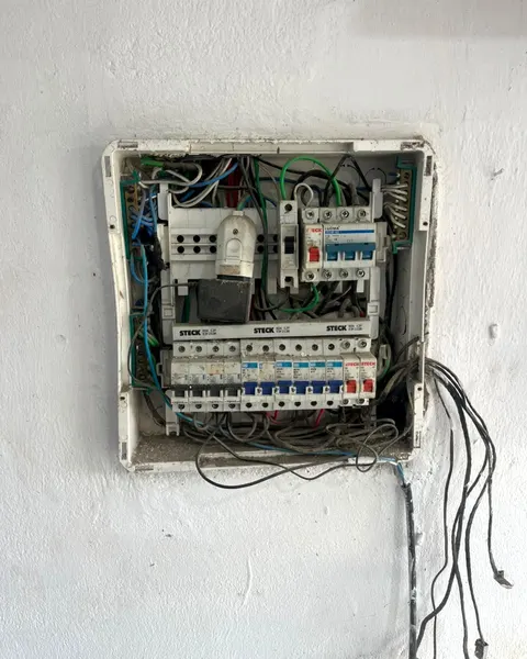 Quadro de distribuição antigo numa parede branca, aberto, com fios soltos pendurados para baixo