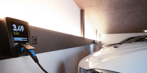 Carregador de carro elétrico na parede, ligado a um carro branco