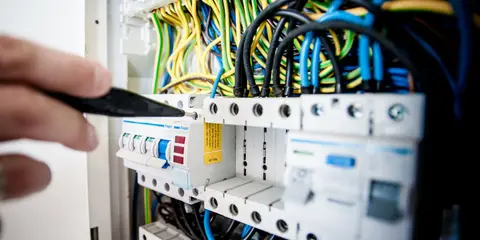 Mão mexendo em disjuntores dentro de um quadro de luz cheio de fios
